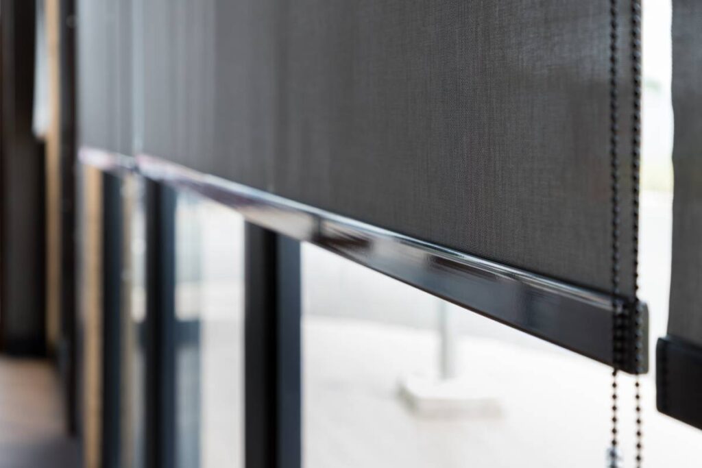 An up-close image of a dark-colored roller shade on a residential window with a beaded loop