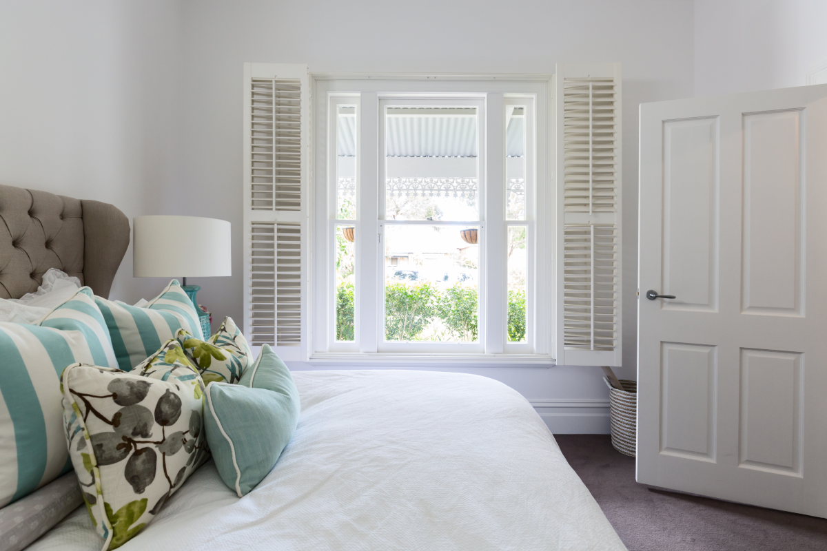 Opened custom interior shutters in a neutral bedroom with pops of blue accents