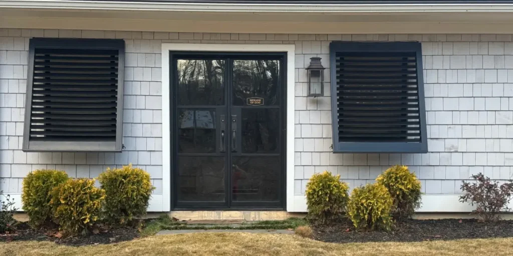 A close-up image of black exterior shutters on windows near a home's front door