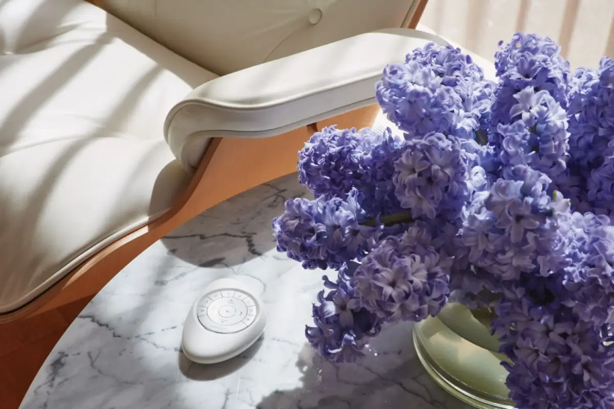 The Pebble® Remote for Hunter Douglas PowerView® Automation sitting on an end table with purple flowers